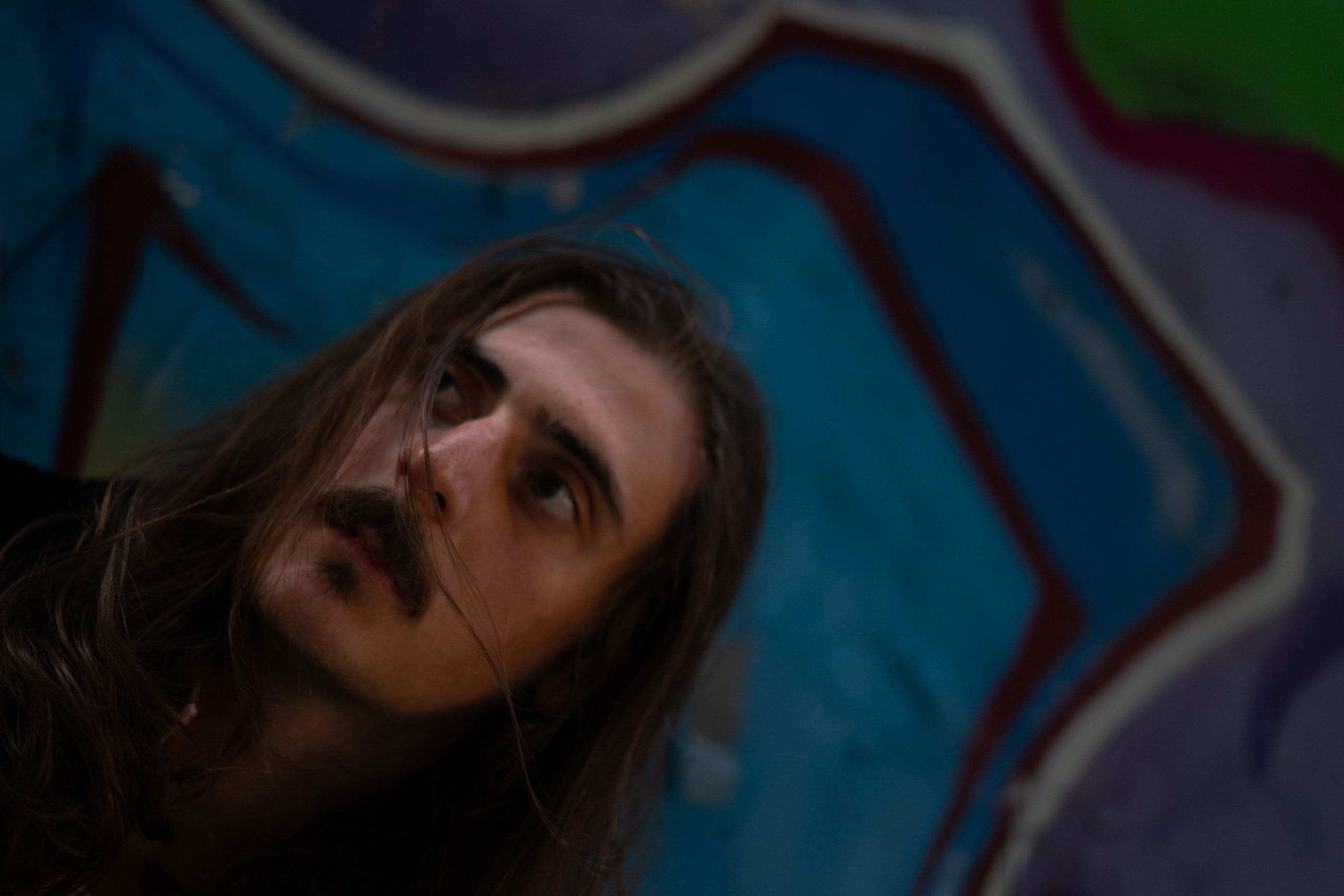 The artist lying against a graffiti wall, looking up